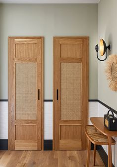 two wooden doors in a room next to a table with a mirror on the wall