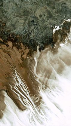 an aerial view of water and land in the ocean, with waves coming up on it