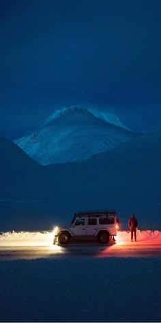 two people standing next to a van in the snow at night with mountains in the background