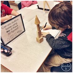 a young boy sitting at a table writing on a piece of paper next to a wooden tower