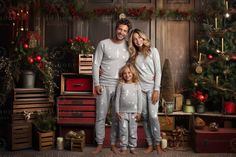 a man and woman standing in front of a christmas tree with their daughter, who is wearing pajamas