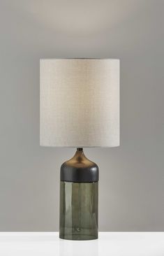 a green glass table lamp with a white linen shade on the base and a grey wall behind it