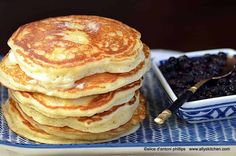 a stack of pancakes sitting on top of a blue and white plate next to a bowl of berries