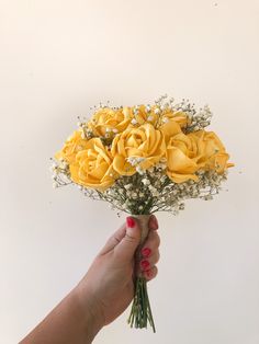 a hand holding a bouquet of yellow roses with baby's breath in the middle