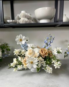 a vase filled with white and blue flowers on top of a table next to shelves