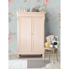 a pink armoire sitting next to a wall with flowers on it and a teddy bear