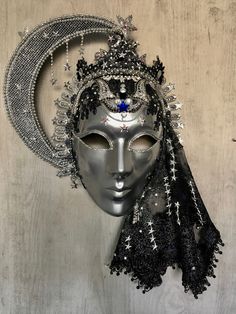 Mozart's opera, "The Magic Flute" was my inspiration for creating my 'Queen of the Night' mask.  Swathed in a silver glittered black which sweeps down to form a star-studded veil, she states formidably beside her hard-lacquered moon of silver net which has been inset with glowing miniature LED lights. These are activated from a switch in the back of the mask  (Batteries are included.)  Her hand-cut black lace crown is heavily embossed silver braid which has been hand-glitzed with Swarovski eleme Maquarade Mask, Blind Masquerade Mask, Mask With Veil, Full Mask Design Ideas, Moon Mask Masquerade, Masquerade Ball Aesthetic Dark, Masquerade Crown, Veil Covering Face, Moon Masquerade Mask