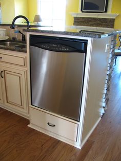 a dishwasher in the middle of a kitchen with yellow walls and wood floors