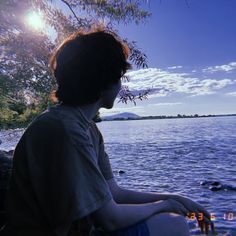 a boy sitting on the edge of a body of water looking out at the ocean