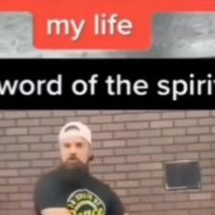 a man standing in front of a brick wall holding a cup and wearing a beanie