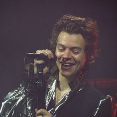 a man holding a microphone in his right hand and wearing a shiny jacket on stage