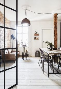 an open living room and dining area with wood flooring, exposed brick wall, white painted walls