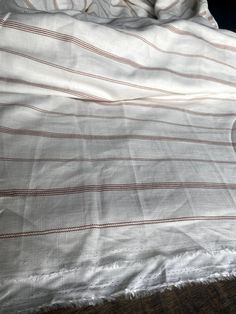 an unmade bed with white and brown striped comforter on it's side