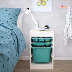 a white nightstand with two blue bins on top of it next to a bed