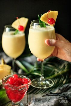 two glasses filled with drinks sitting on top of a table next to pineapples