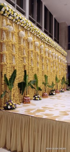 a long table with flowers on it in front of a large wall made out of yellow and white cloths