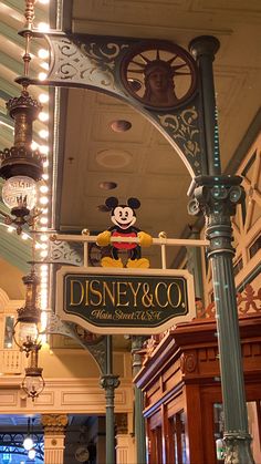 a mickey mouse sign hanging from the side of a light pole in a building with lights on it