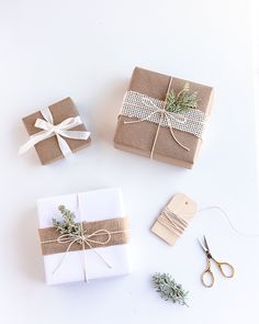 three wrapped gift boxes tied with twine and some scissors on a white surface next to each other