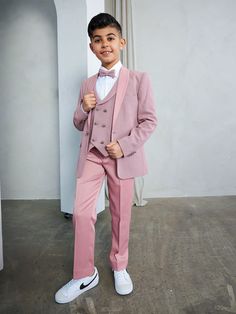 a young boy wearing a pink suit and bow tie standing in front of a white wall