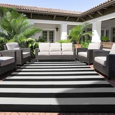 an outdoor living area with black and white striped rugs, wicker furniture and potted plants