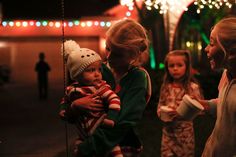 three girls and one boy standing outside at night with christmas lights on the trees in the background