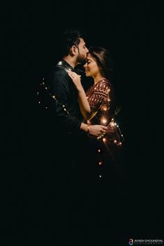 a man and woman standing next to each other in the dark with lights on them