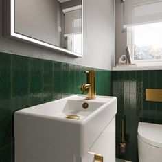 a white sink sitting next to a toilet in a green and white bathroom with gold faucet