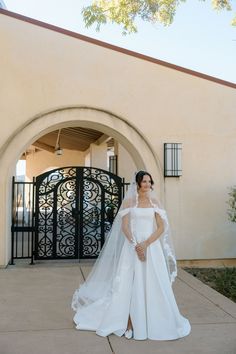 a woman standing in front of a building wearing a wedding dress with a veil on her head