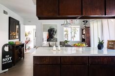 a kitchen with white counter tops and wooden cabinets in front of a painting on the wall