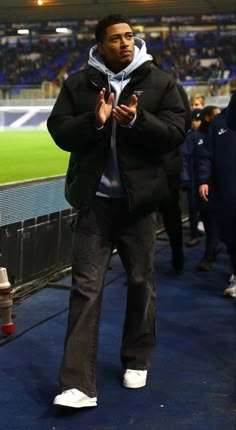 a man in black jacket and white sneakers walking on blue carpeted area at stadium