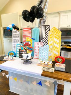 a table topped with lots of cupcakes next to balloons and paper cutouts