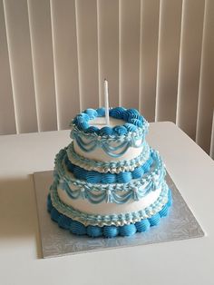 a blue and white three tiered cake with a single candle on top, sitting on a table