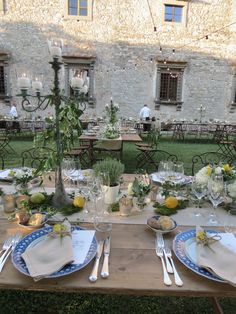 the table is set with plates and silverware for an outdoor dinner in front of a stone building