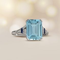 This elegant aquamarine ring features a fleur-de-lis on each shoulder, adorned with four round brilliant cut diamonds and three calibre French-cut sapphires. The center aquamarine weighs approximately 5.40 carats and is emerald-cut. This platinum ring is decorated with an open-work under-gallery.
The measurements of the center gemstone are 12mm x 9mm. This ring’s profile is as low as the depth of the gemstone.
This ring can be resized to any finger size at no extra cost.
Ready to Make It Yours? Elegant Sapphire Ring With Diamond Side Stones, Elegant Blue Topaz Ring With Diamond, Classic Blue Sapphire Ring With Gemstone Accents, Classic Topaz Ring With Diamond And Gemstone Accents, Formal Sapphire Ring With Diamond Side Stones, Platinum Blue Topaz Ring With Diamond Accents, Blue Topaz Ring With Accent Stones In Platinum, Elegant Diamond Topaz Ring With Gemstone Accents, Elegant Blue Topaz Ring For Formal Occasions