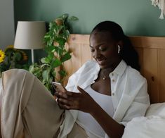 a woman sitting on a bed looking at her cell phone