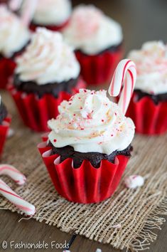 red velvet cupcakes with white frosting and candy canes on a table