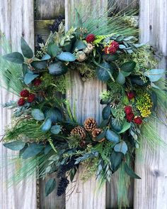 a wreath is hanging on the side of a wooden fence with greenery and pine cones