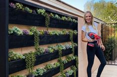 a woman standing next to a wall with succulents growing on it