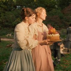 two women in historical dress holding a cake