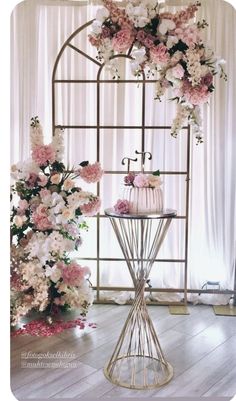 a wedding cake on a stand with pink and white flowers in front of a window