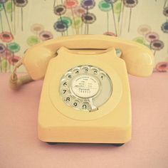 an old yellow phone sitting on top of a pink table next to a floral wallpaper