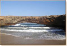 an arch in the rock that is over looking the water and beach with waves crashing on it