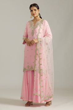 Pink kurta with silver floral embroidered motifs highlighted by cutdana and scalloped borders. Comes with sharara and dupatta.
Components: 3
Pattern: Embroidered
Type Of Work: Sequin,Cutdana
Neckline: Notched
Sleeve Type: Three quarter
Fabric: Georgette,Net
Color: Pink
Other Details: 
Cut-out borders
Gota detail
Attached lining
Closure: Sharara: Elasticated waistband
Occasion: Mehendi and Haldi,Sangeet - Aza Fashions Pink Embroidered Chinon Sharara, Pink Embroidered Sharara In Chinon Fabric, Fitted Pink Sharara With Printed Motifs, Pink Embroidered Sharara With Straight Kurta, Pink Semi-stitched Sharara With Intricate Embroidery, Types Of Work, Sharara Set, Three Quarter, Aza Fashion