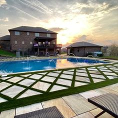 an empty swimming pool surrounded by grass and lawn furniture with the sun setting in the background