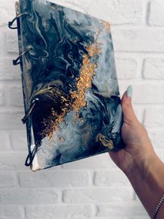 a hand holding an art journal with gold flecks and black marbled paper