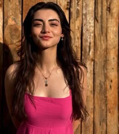 a woman in a pink dress standing next to a wooden fence with her eyes closed