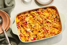 a casserole dish with cheese and vegetables in it on a table next to silverware