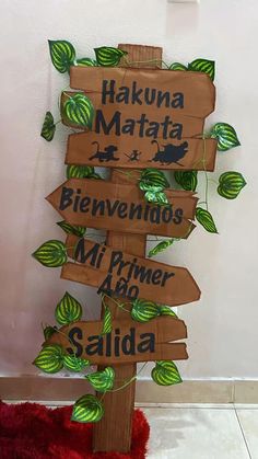 a wooden sign sitting on top of a red rug next to a white wall with green leaves