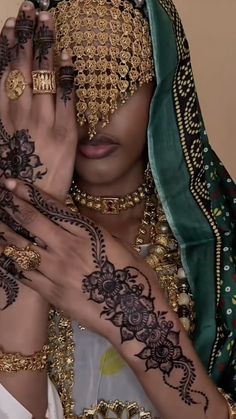 a woman with henna on her face and hands covered in gold, black and green jewelry