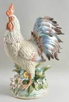 a rooster figurine sitting on top of a flowery base with flowers around it